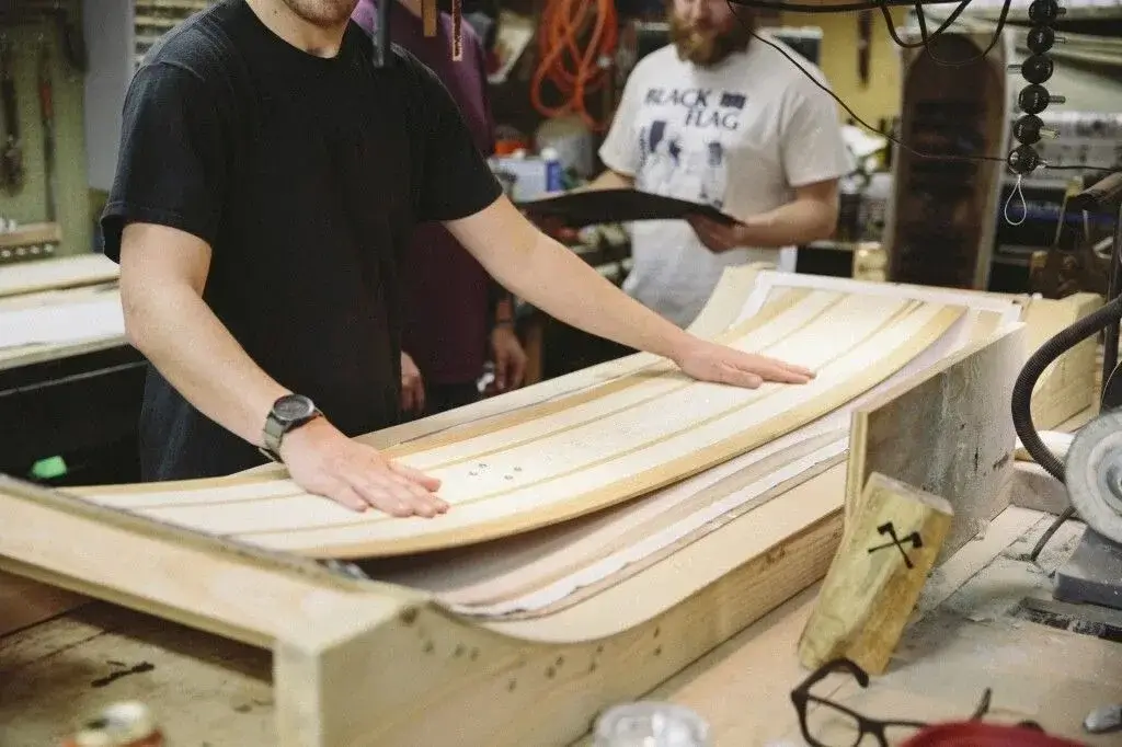 A technician carefully crafting a snowboard prototype in a workshop.