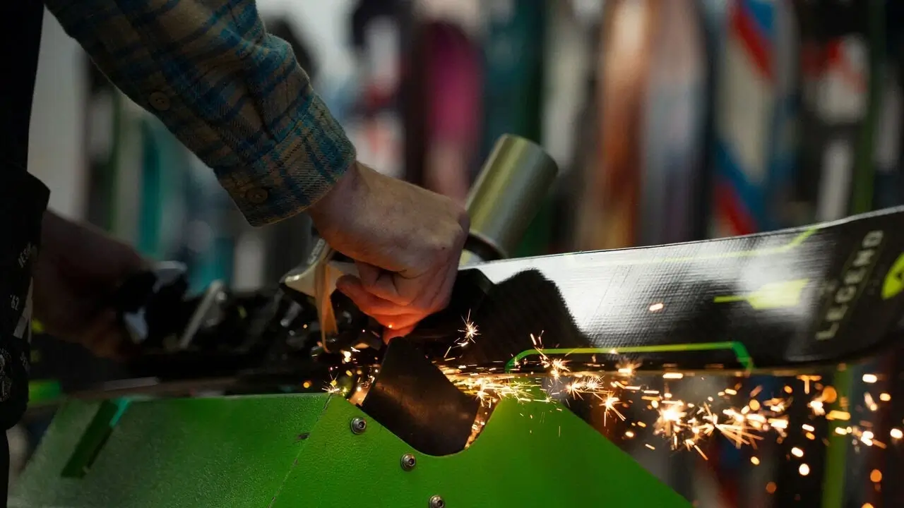 Close-up of an expert technician tuning the edge of a ski with a specialized tool.