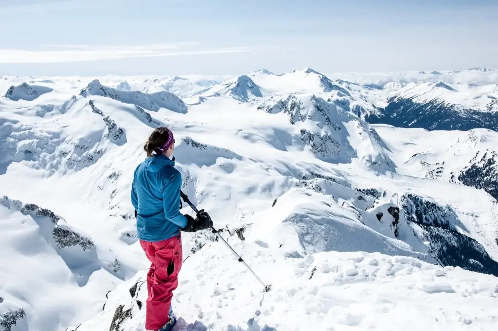 A lone skier on a ridge overlooking a valley.